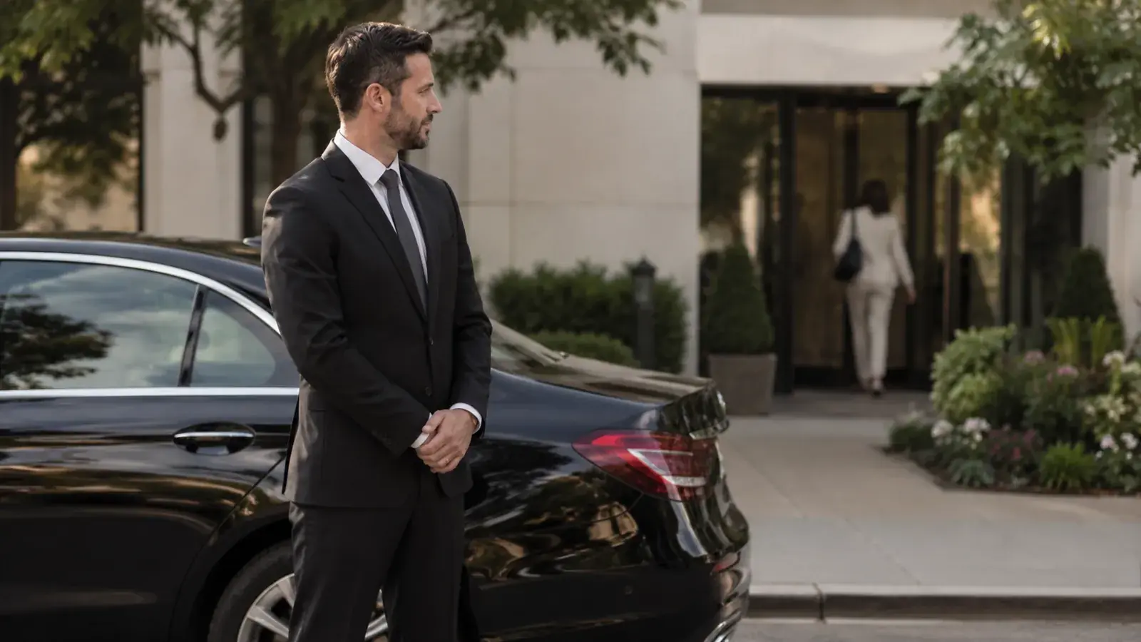 Private driver waiting beside a client's car outside a medical center.