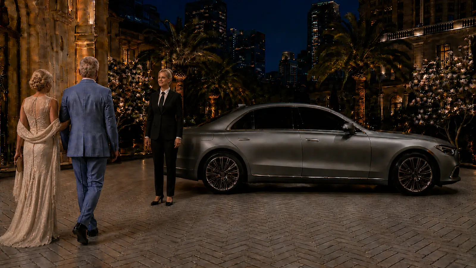 Private driver welcoming formally dressed guests beside a silver sedan at an evening event.