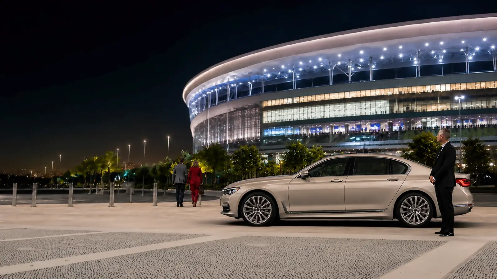 Private driver and gold sedan ready outside a stadium after a sporting event.